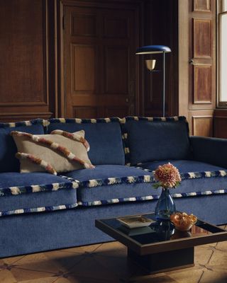 blue sofa with tufted trim in a living room with decorative wall panelling and square coffee table