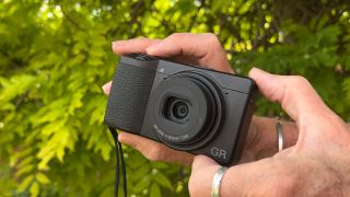 Ricoh GR III HDF being held between a man's hands outdoors