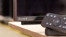 The corner of a Sony TV with a remote sitting on a TV stand