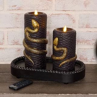 Martha Stewart Set of 2 Embossed Snake Flameless Pillar Candles against a brick wall.