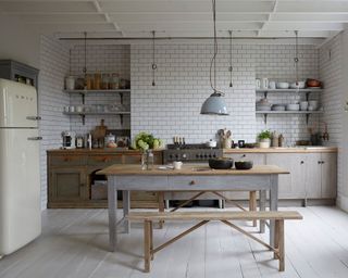 Modern kitchen with white tiles, white wood flooring, gray wooden kitchen cabinets, wooden dining table in center or room, cream smeg fridge on left hand side