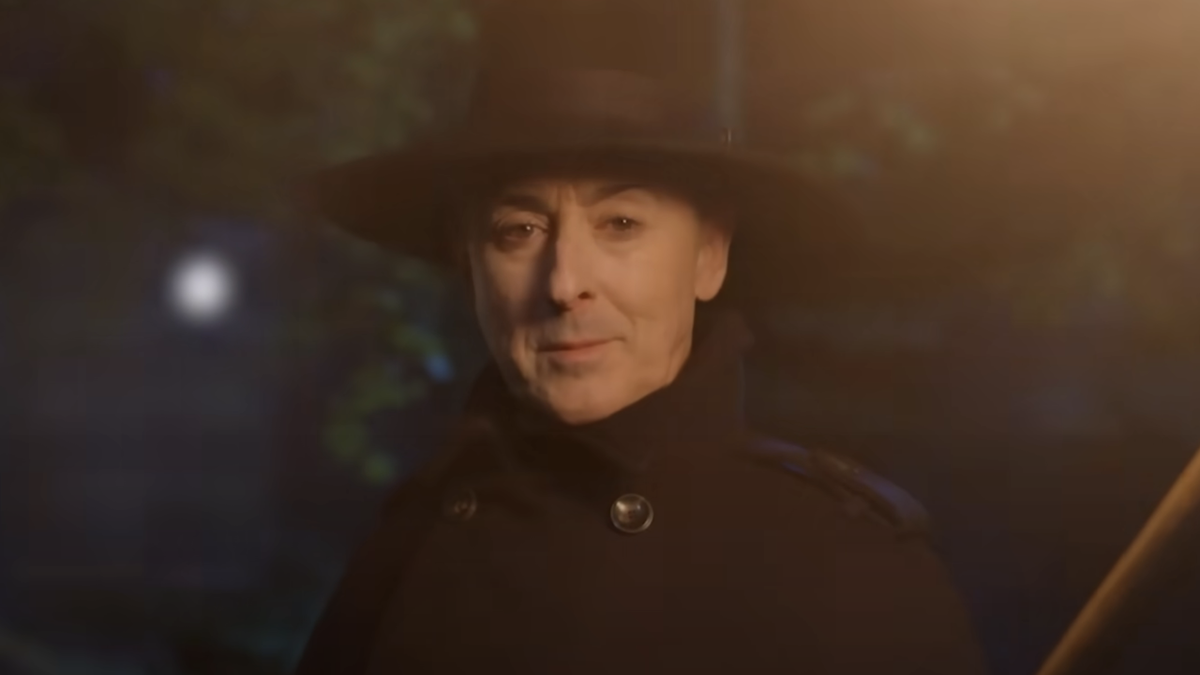 Alan Cumming in black peacoat and hat with torch in The Traitors