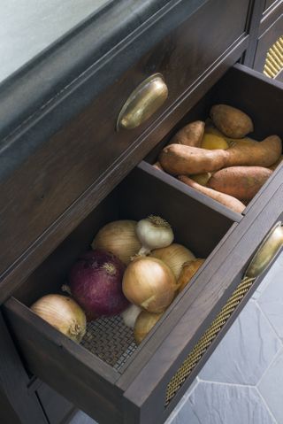 Close of shot of onions, garlic, and sweet potatoes in a chic produce storage drawer