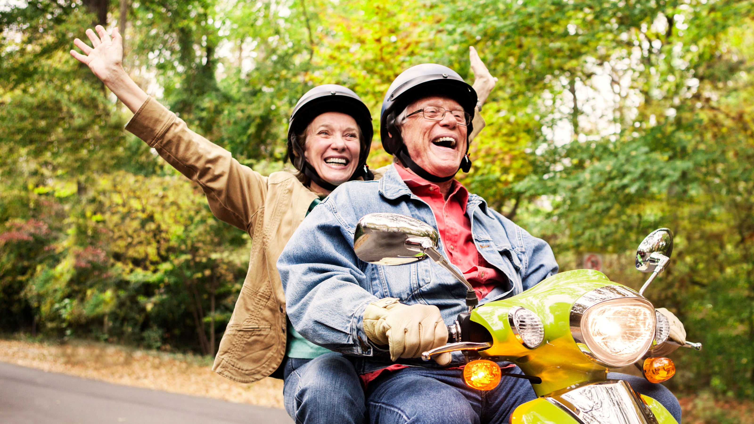 Older white couple on a scooter smiling and having fun