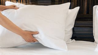 A person stacks two white bed pillows on a bed