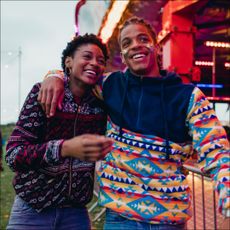 Young couple are laughing and talking as they walk around a funfair on a date