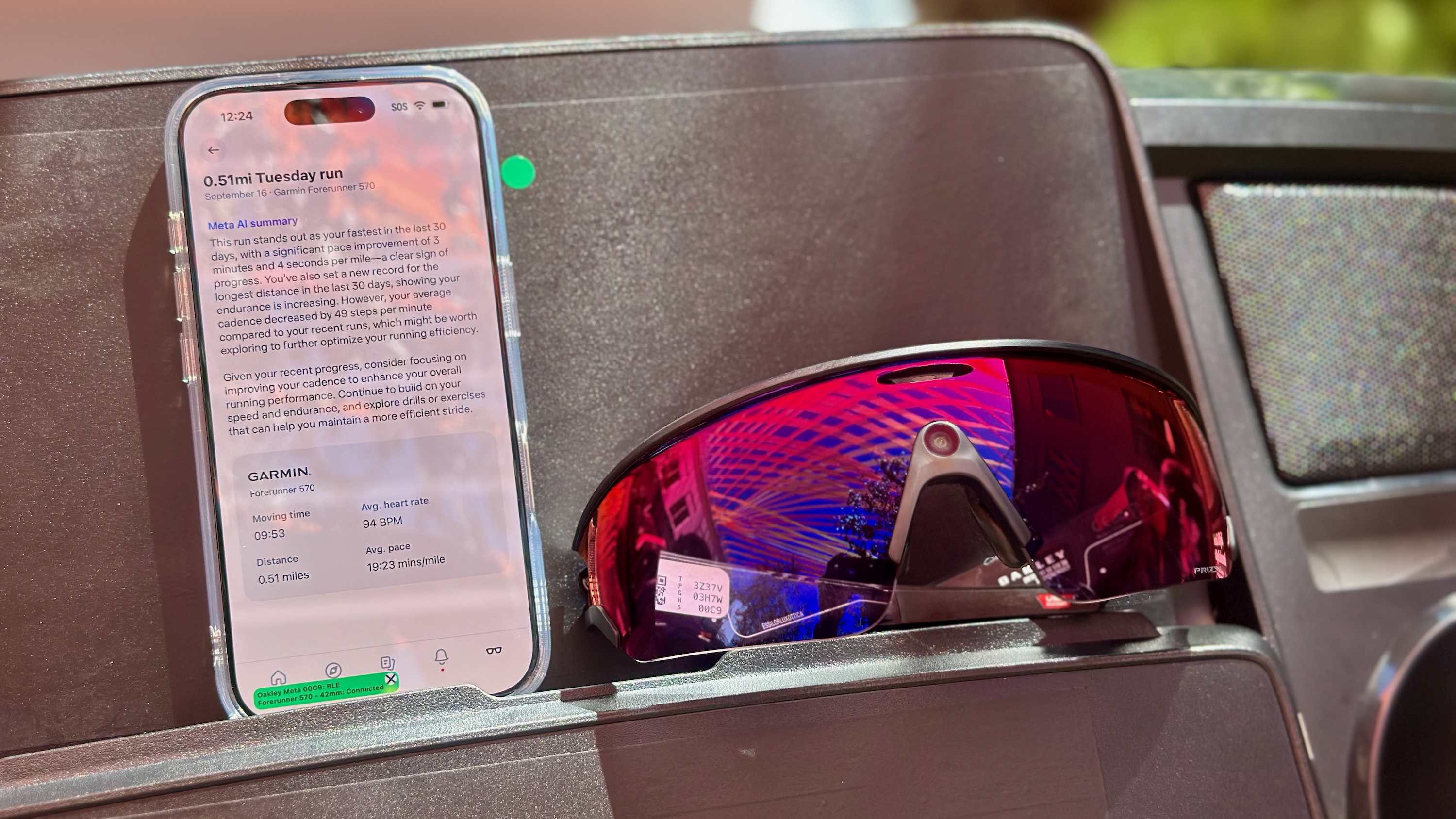 Photo of the Oakley Meta Vanguard smart glasses sitting on a treadmill next to a phone showing a Meta AI workout summary.