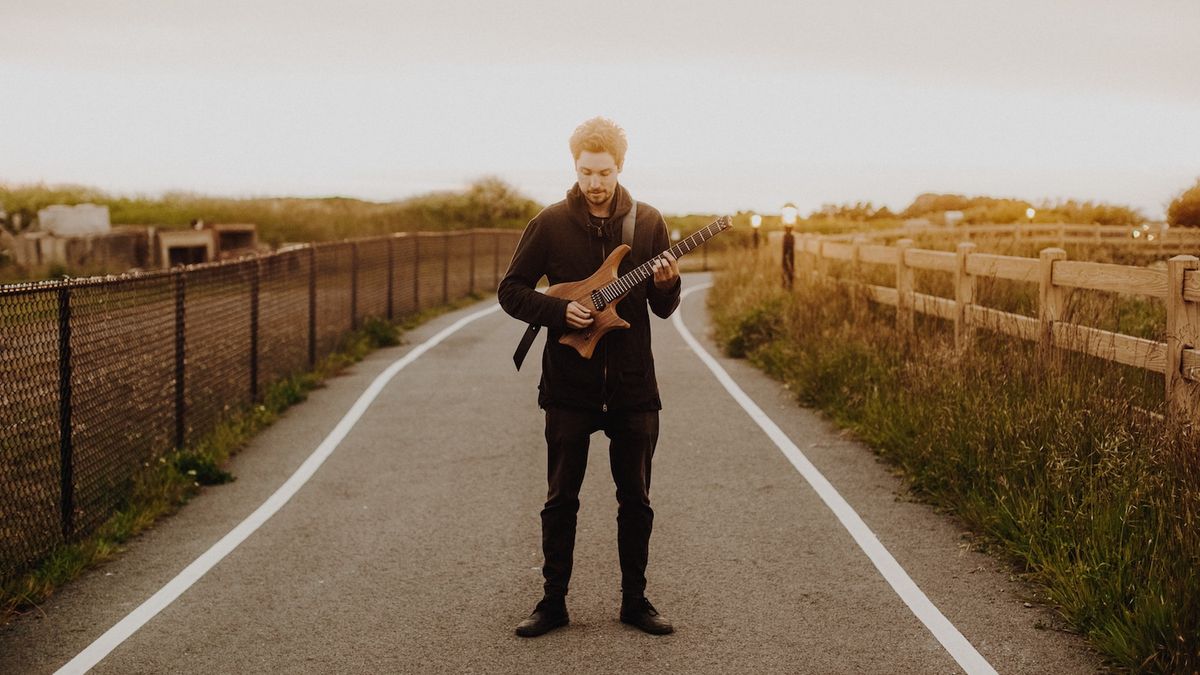 Guitarist Plini poses with his guitar in the middle of a road