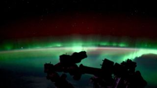 A green aurora simes over the curvature of Earth, seen from a low orbit.