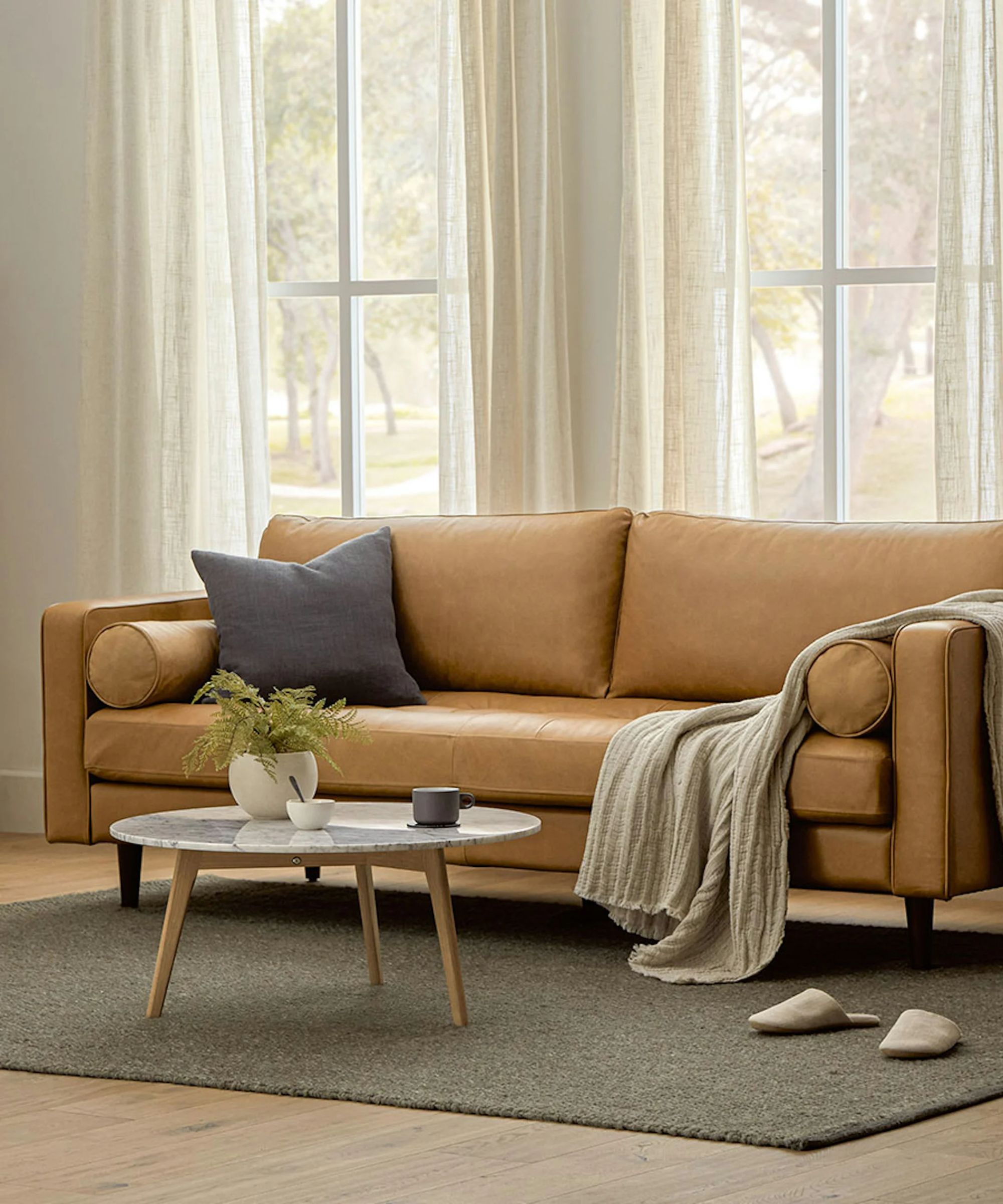 leather couch in a neutral living room with a grey rug and marble and wood round coffee table