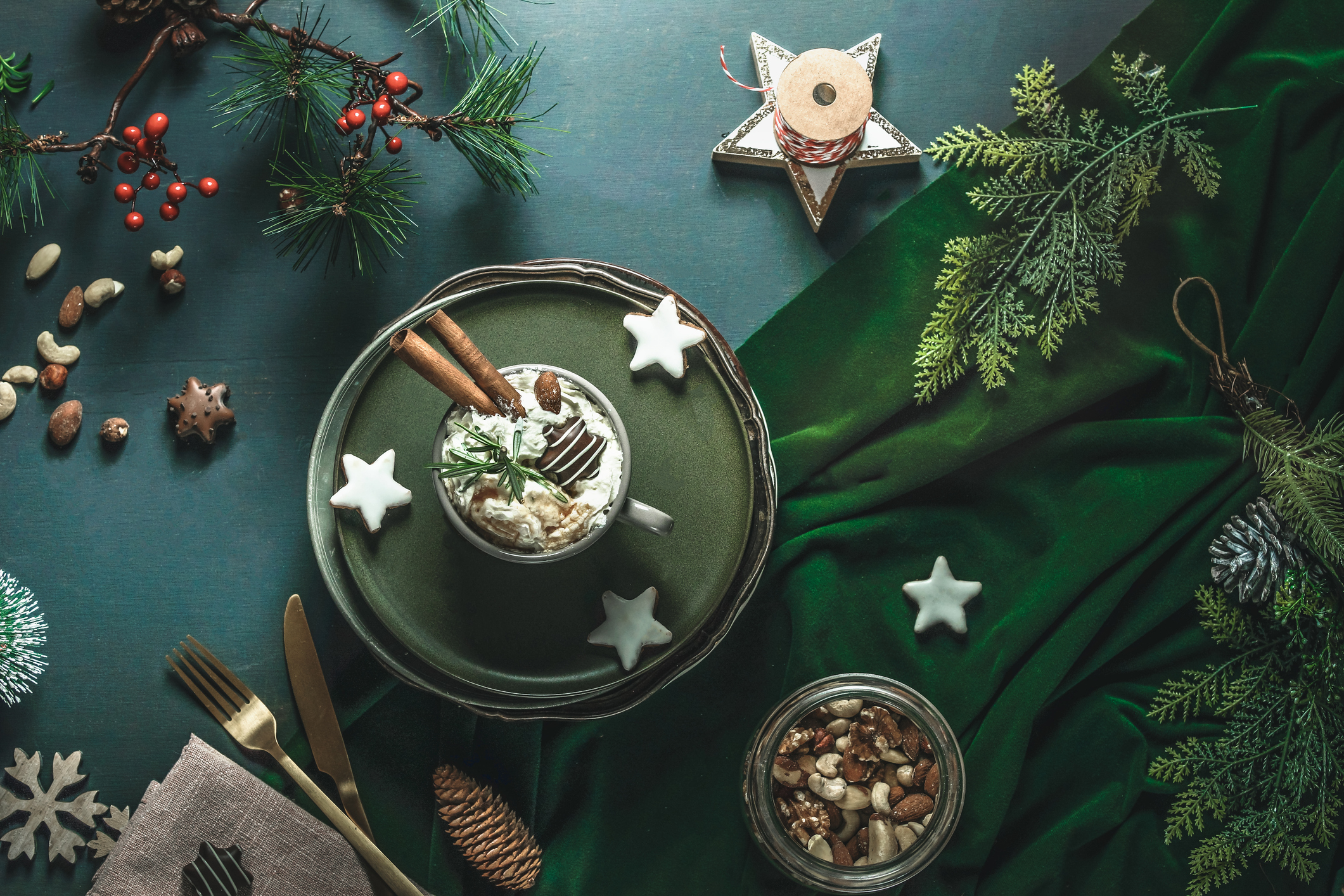 A festive, green set-up with a hot chocolate in the centre with cinnamon sticks, surrounded by stars, and festive foliage.