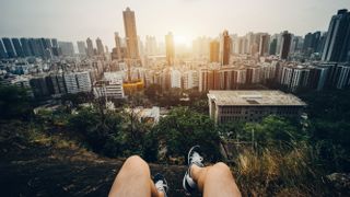 man sitting on the top of mountain watching beautiful sunrise over urban cityscape