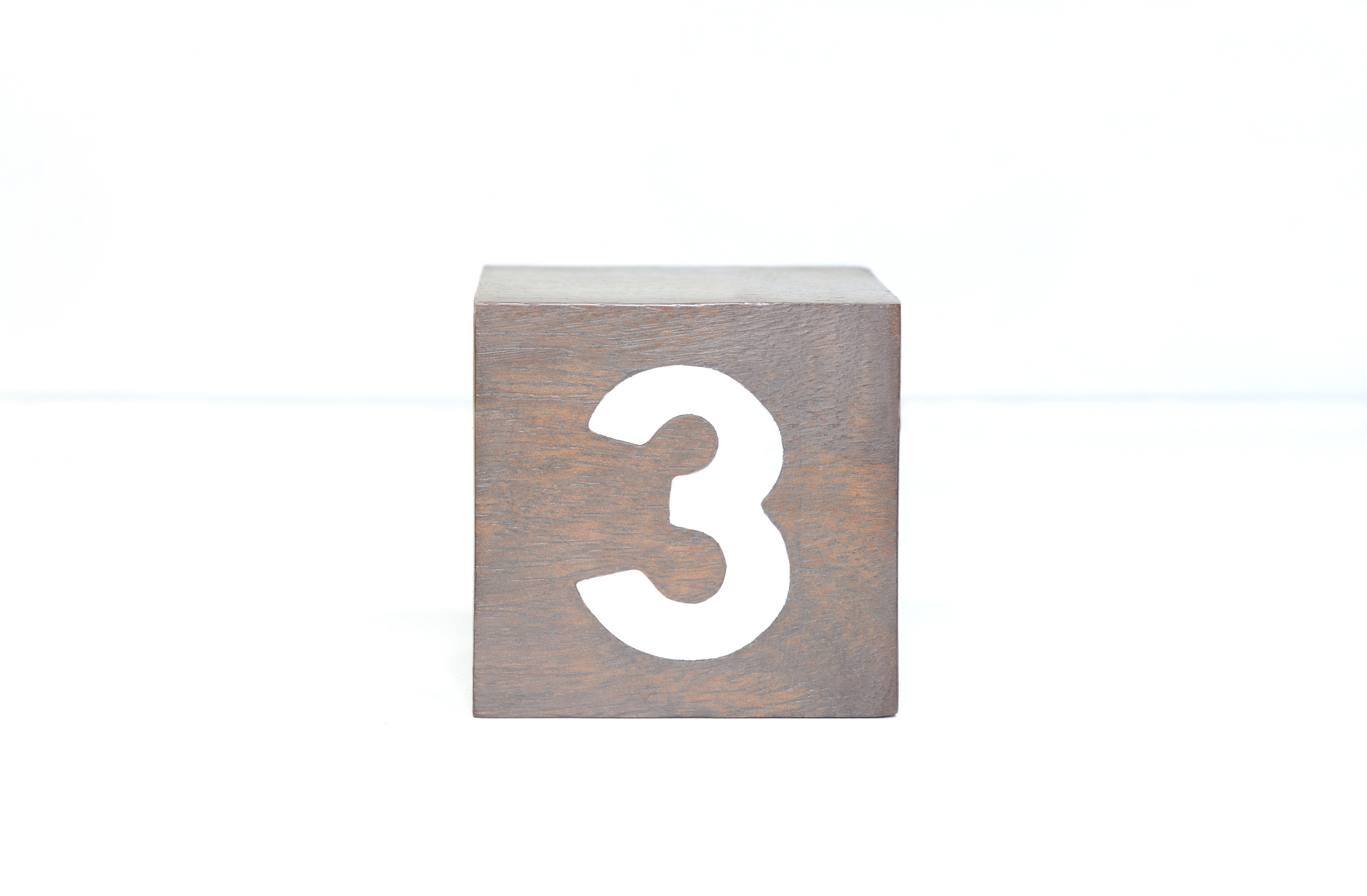Closeup view of silver plated number three on a wooden block.