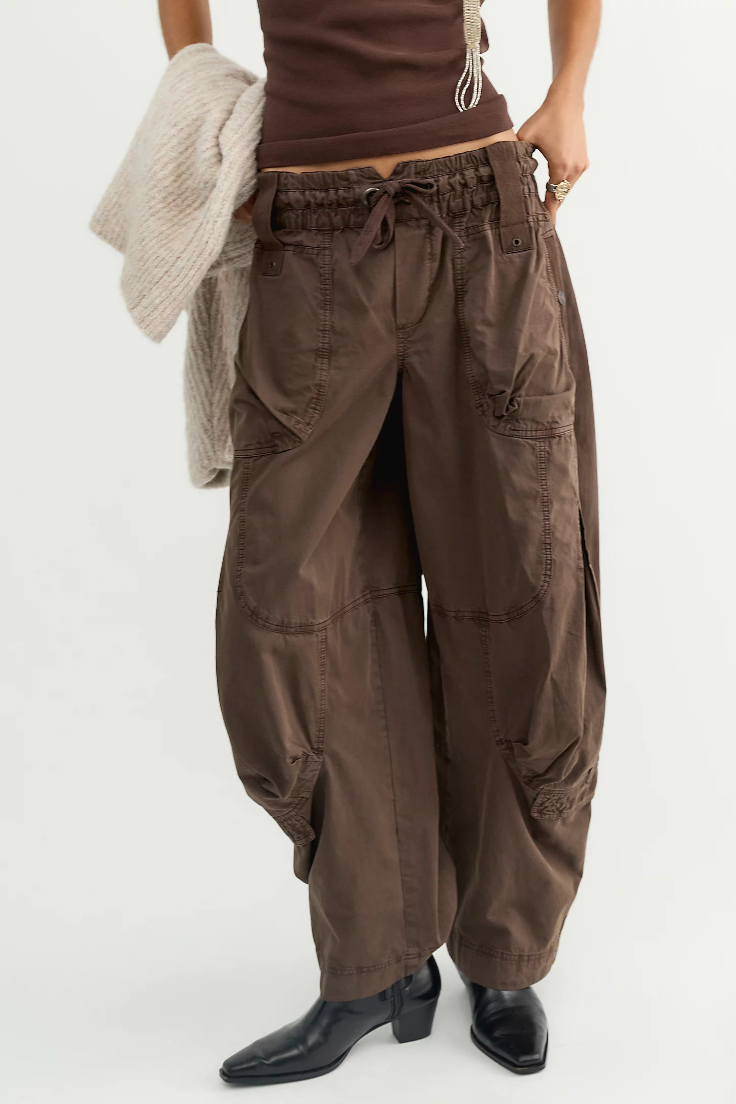 An image of a model wearing baggy brown cargo trousers with black boots and a brown vest