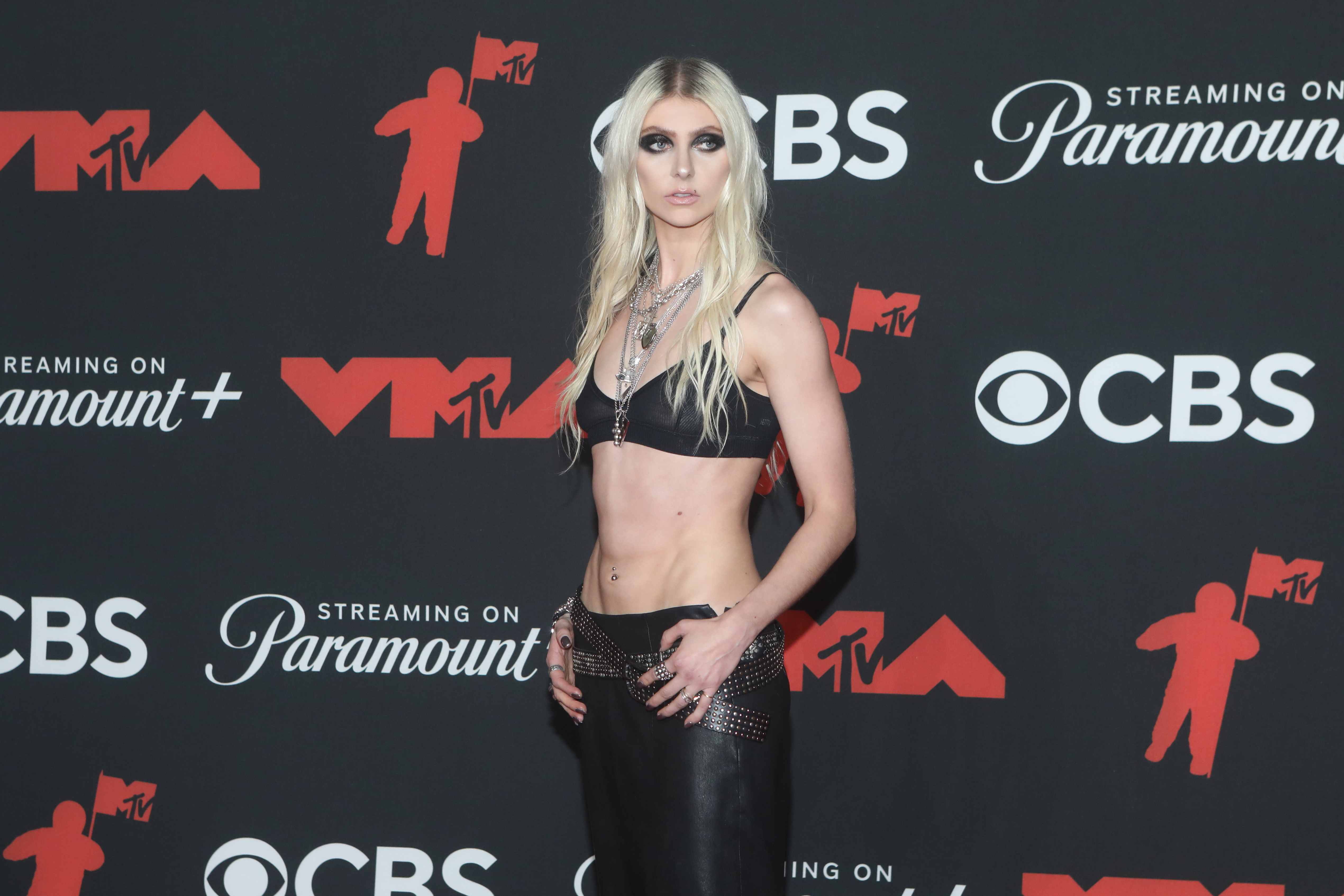 a woman with blonde hair wearing an all black outfit in front of a black, red, and white background