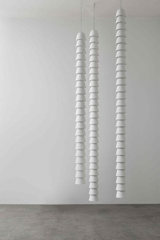 three vertical stacks of bell shaped white objects hanging from a white ceiling photographed against a white wall