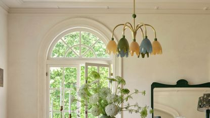Merve Kahraman x Anthropologie multi-color, multi-shade chandelier in a sunlit dining room featuring flowers, taper candles, and a decorative mirror