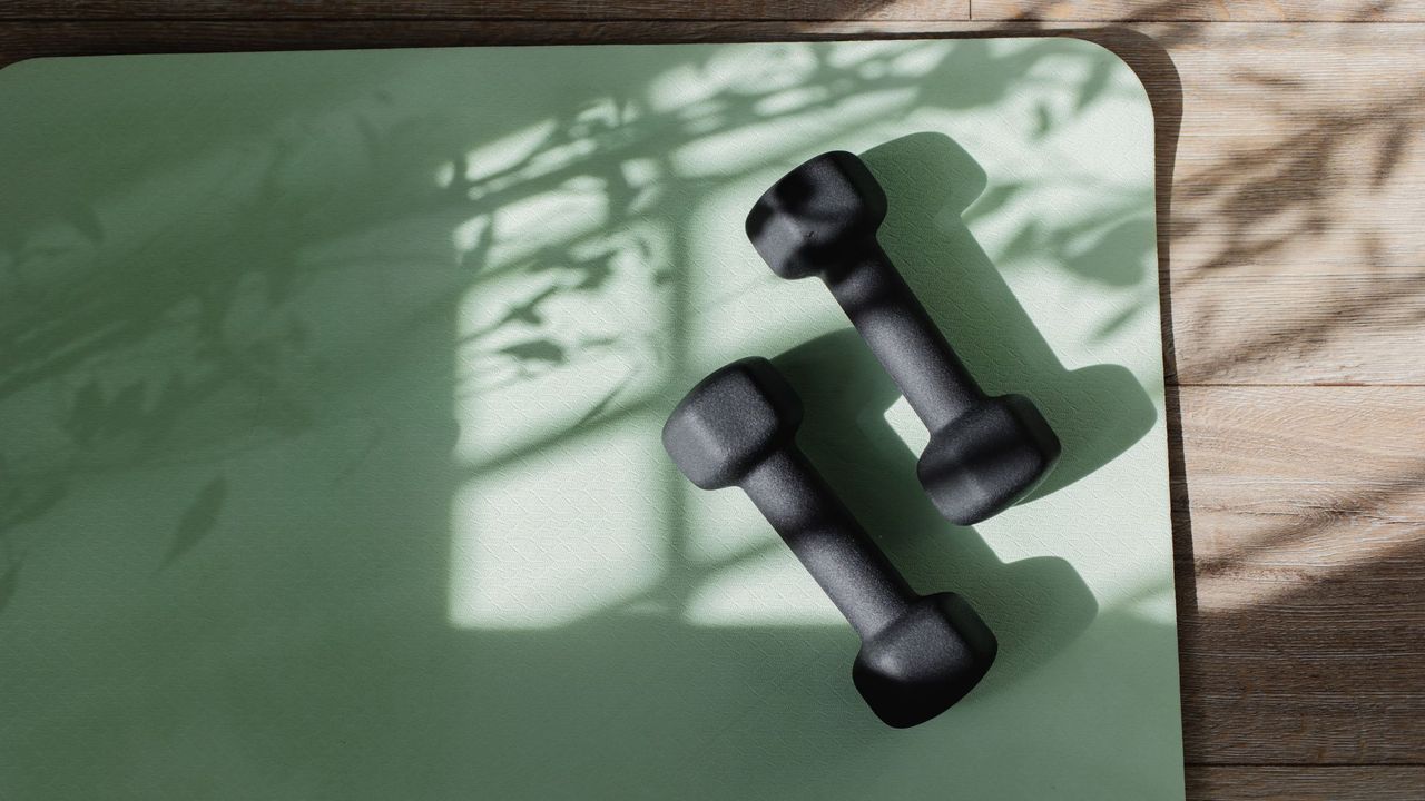 Two dumbbells on a green workout mat for use during a ten-minute Pilates workout