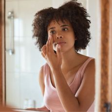 morning skincare routine - woman applying face cream in the mirror - gettyimages-1464166549
