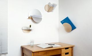 Corner of a room with white walls featuring different variations on hanging fixtures: a shelf, a valet tray, a book stand, a magazine stand, and a peg with glass of water on a brown dressing table against the wall