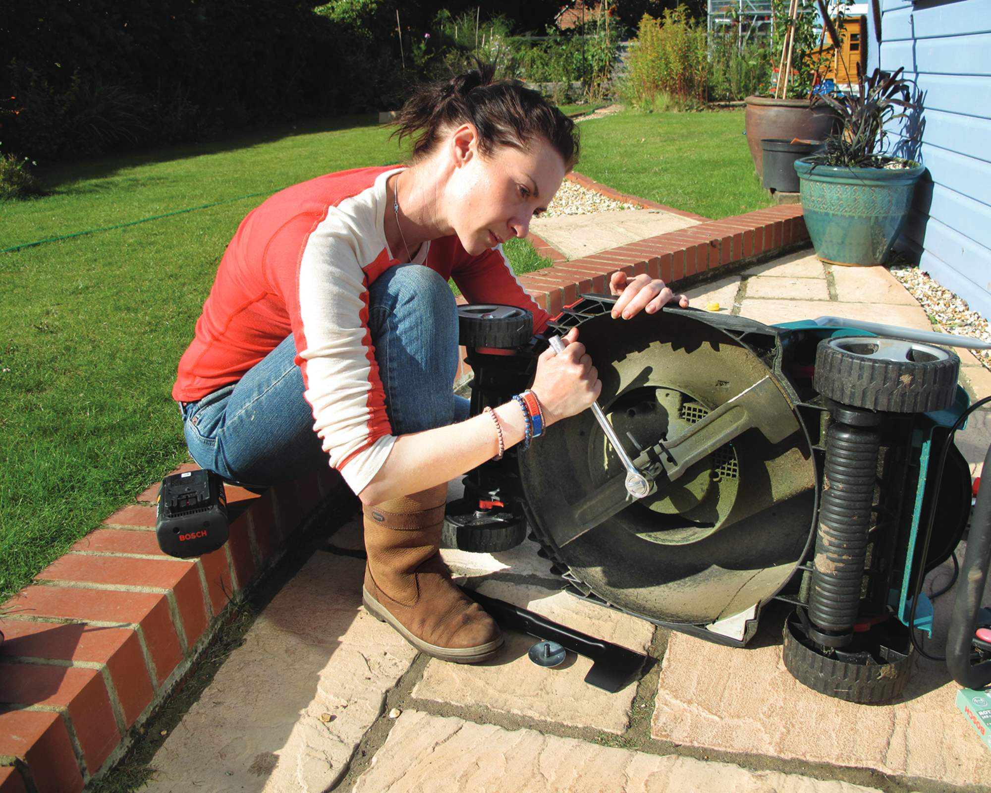 woman replacing an old lawn mower blade on her lawn mower, on a garden patio