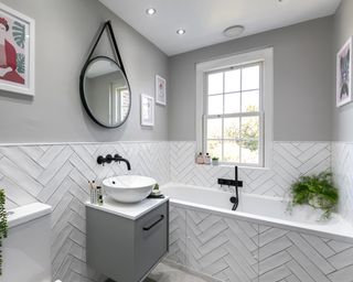 A master bathroom with a white herringbone tiled fitted bath and black faucets