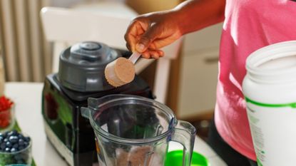 Person placing scoop of protein powder into a blender