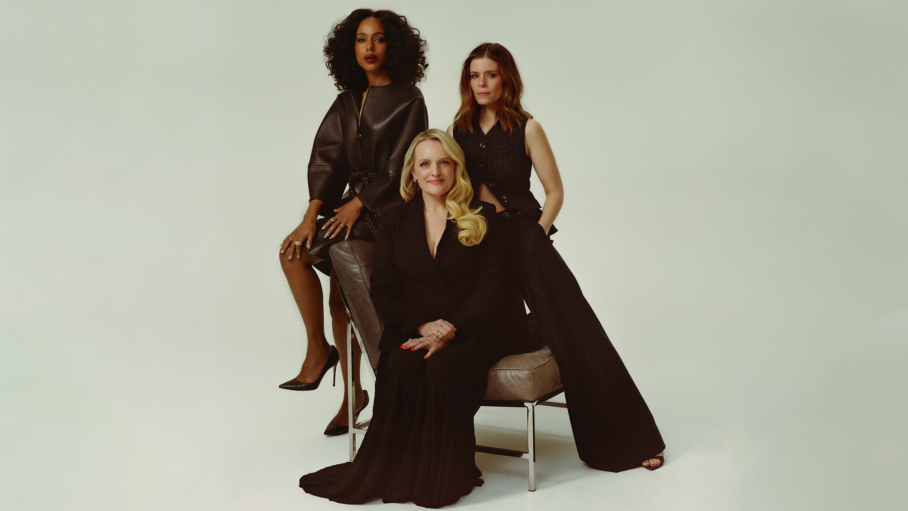 Kerry Washington, Elisabeth Moss, and Kate Mara pose in chic black outfits against a minimalist studio background.