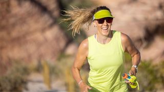 Woman wearing running kit, holding water bottle and sunhat during marathon