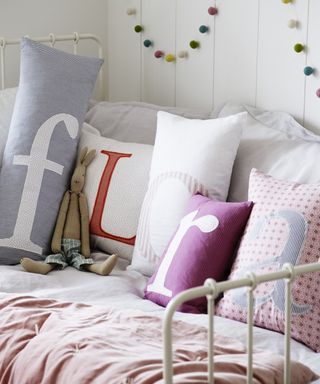 Pastel colored personalised cushions on a daybed spelling out the name 'Flora'.