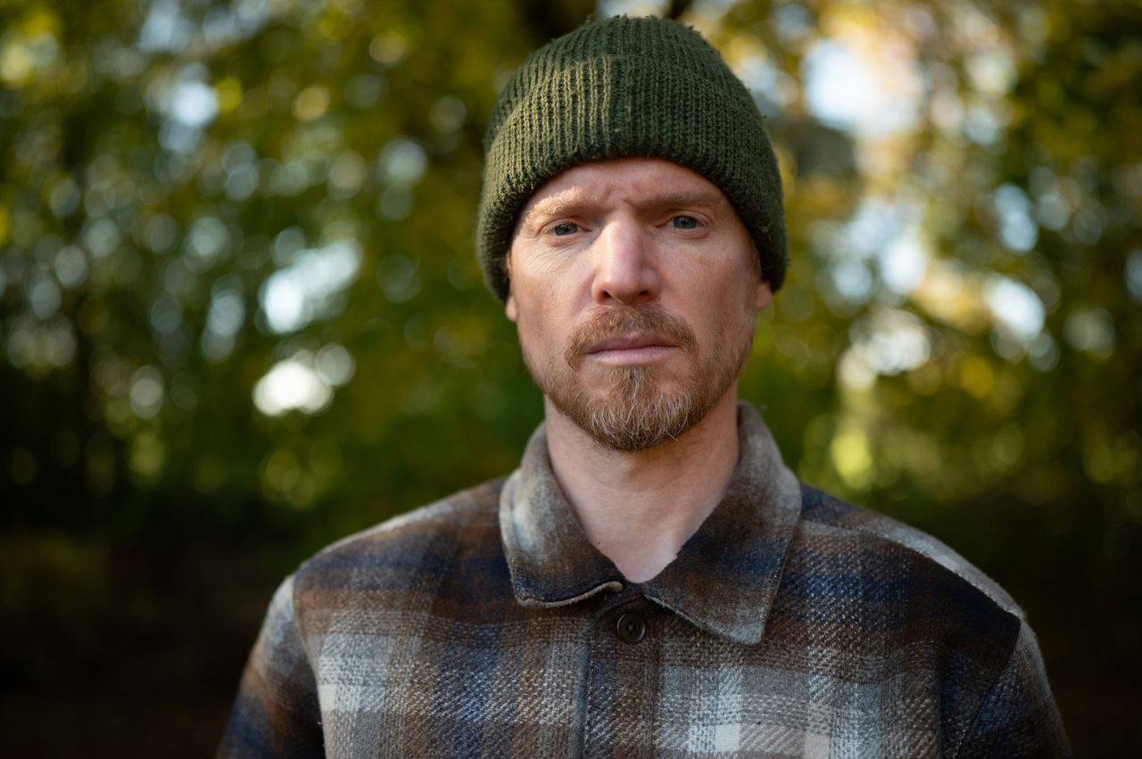 Portrait of a man in a shacket and beanie hat, outdoors with fall trees backdrop