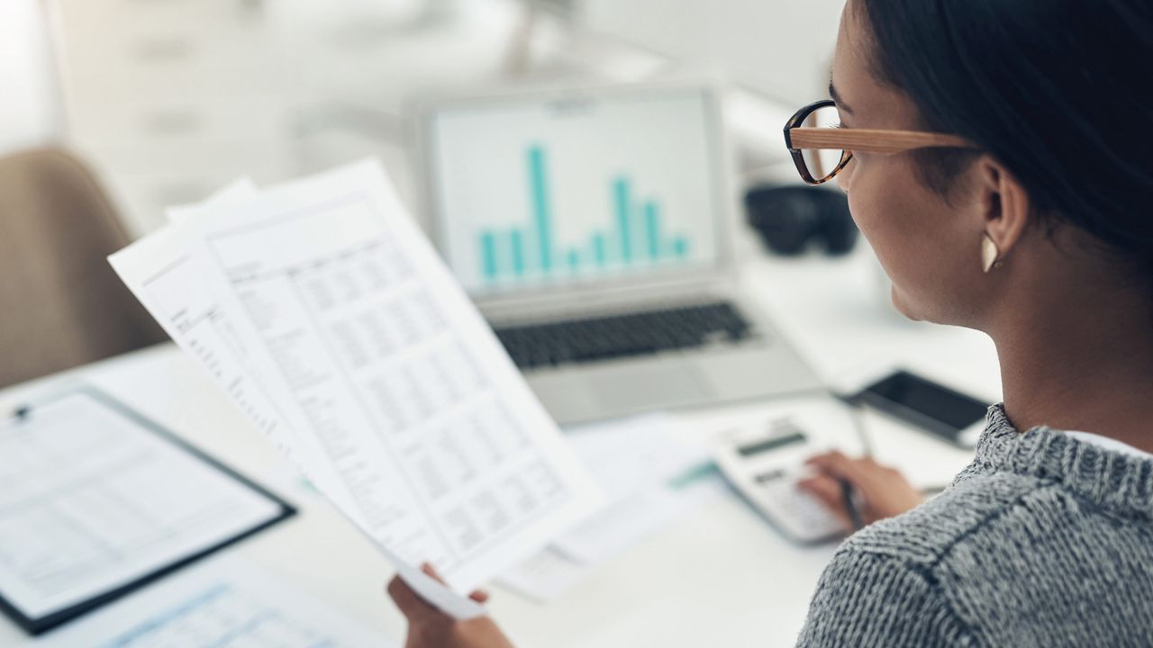 A woman sitting at a desk looks over some papers and bar charts.