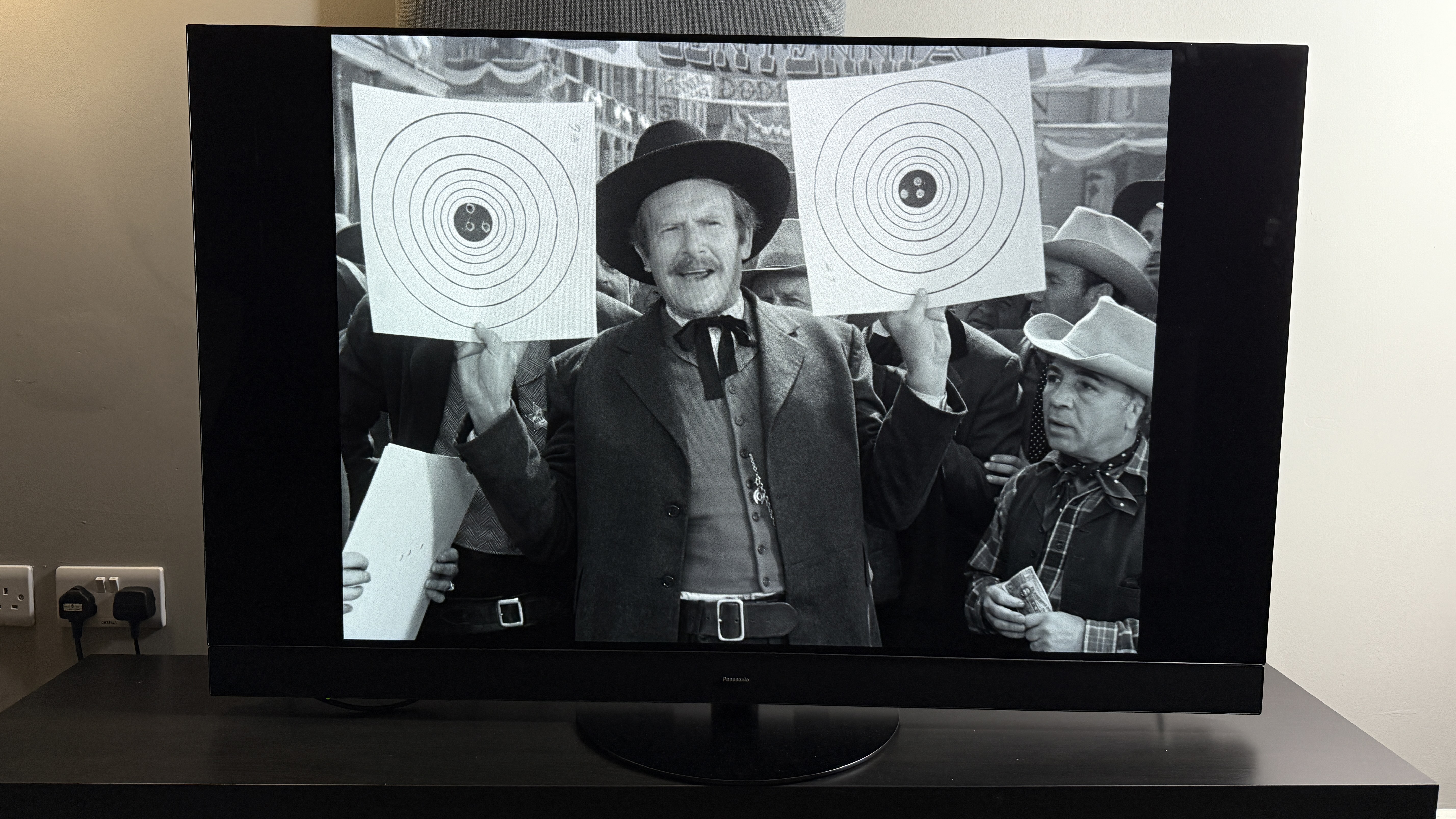 A TV showing the movie Winchester '73, a man holds up two targets from a shooting competition on-screen