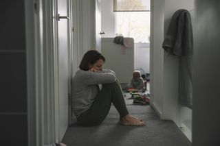 lonely mum sat on floor with baby in background