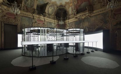 A clock-making workshop set up in the Milan’s Palazzo Visconti. The workshop is surrounded by harsh reflector lights, while the rest of the space is dark.