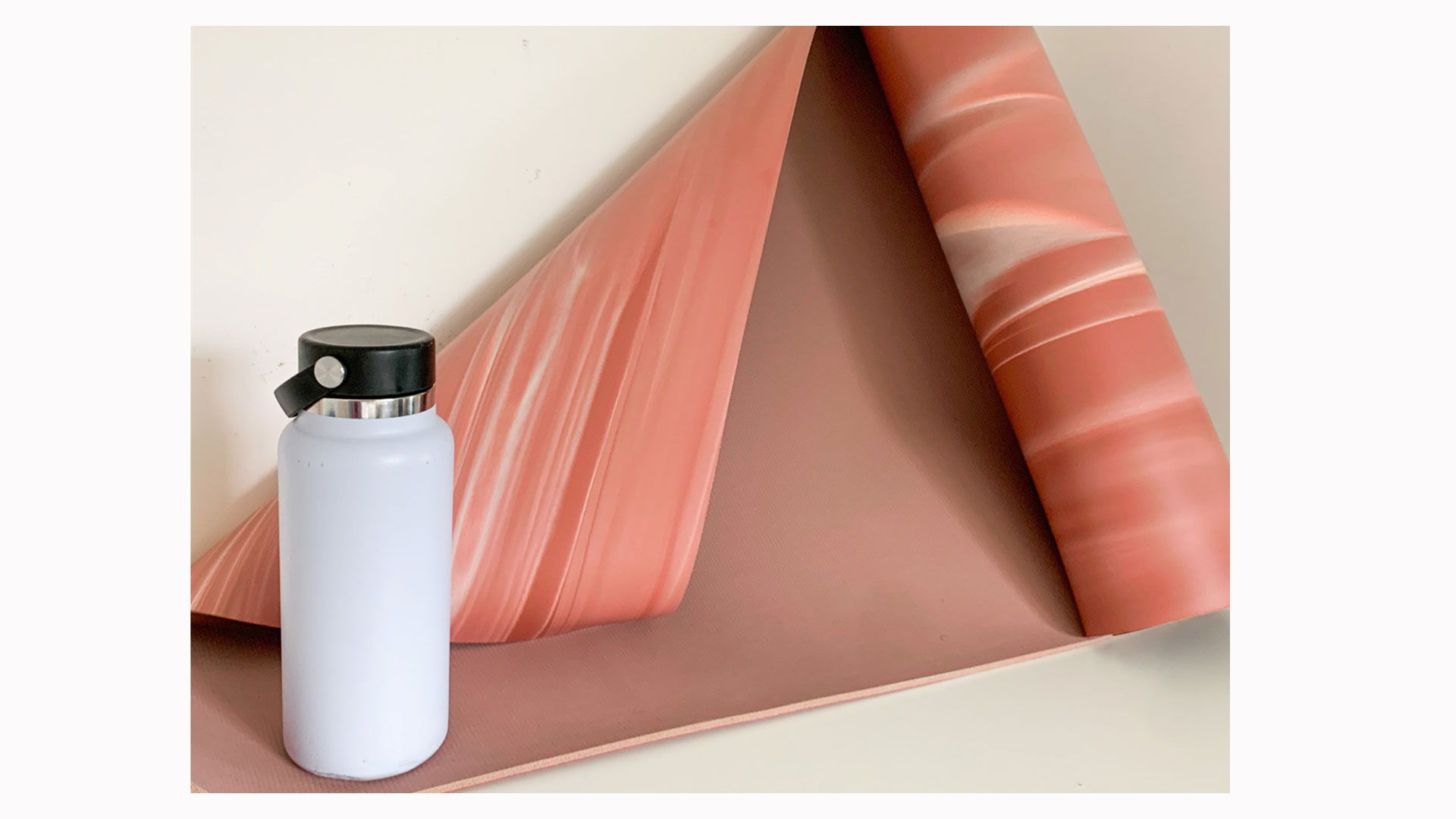 Das Bild zeigt eine halb ausgerollte rosa Lululemon Wende-5-mm-Yogamatte neben einer weißen Wasserflasche aus Metall.