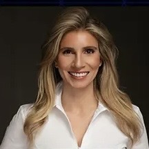 A blonde woman in a white shirt is smiling.