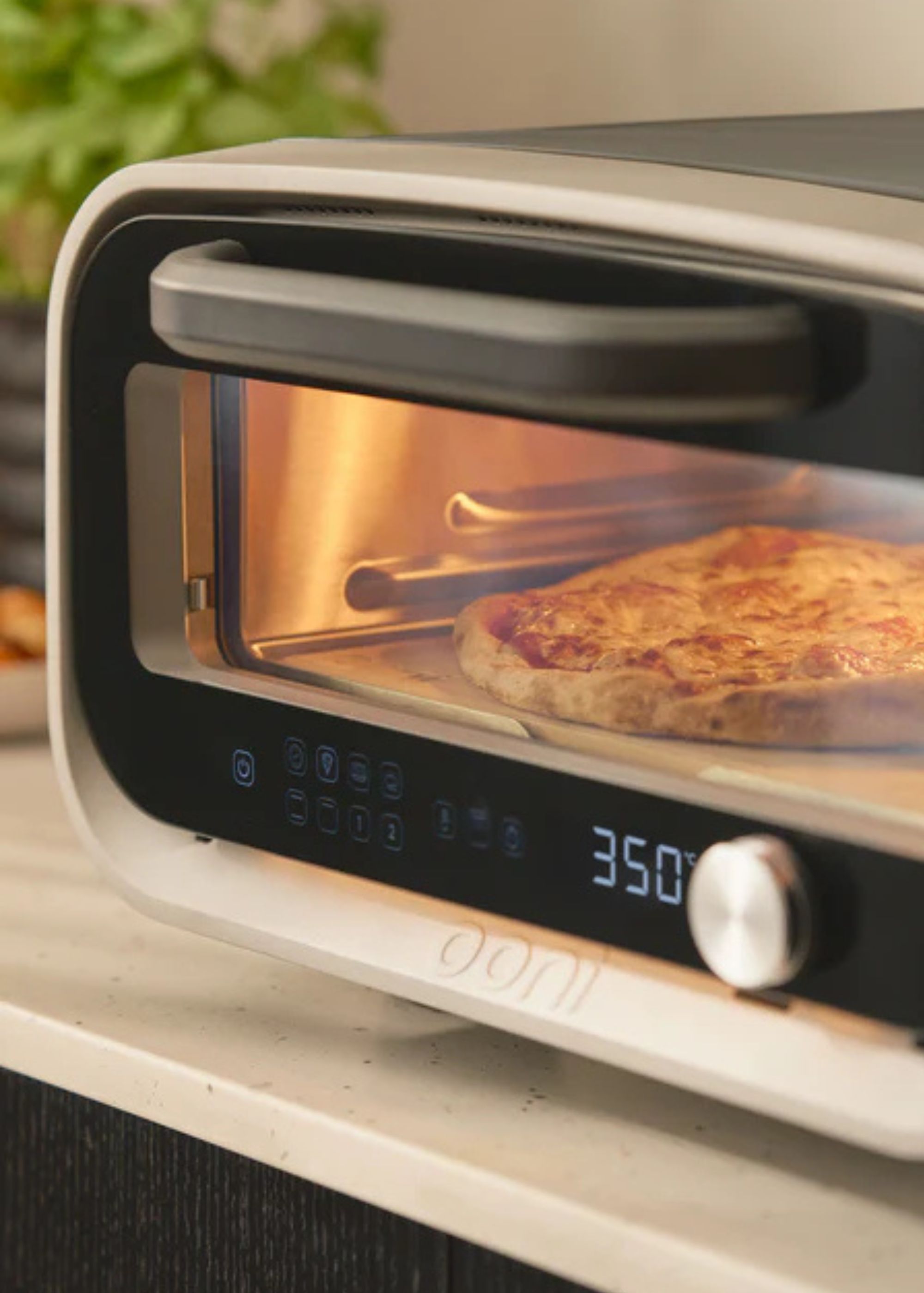 Ooni volt 2 pizza oven up close showing a temperature of 350 degrees on the panel with the oven light on as a pizza cooks inside on the countertop