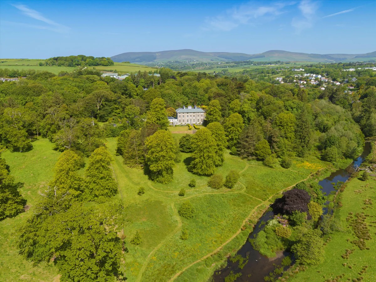 An aerial view of a grand country home in some parkland on the isle of man. A river runs through the foreground