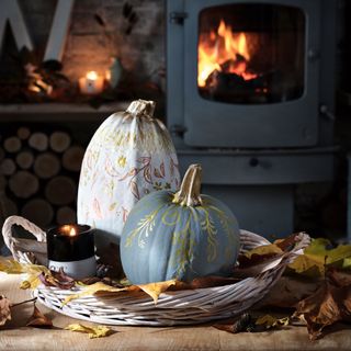 two pumpkins decorated with gold paint sitting on a wicker tray beside a woodburning stove