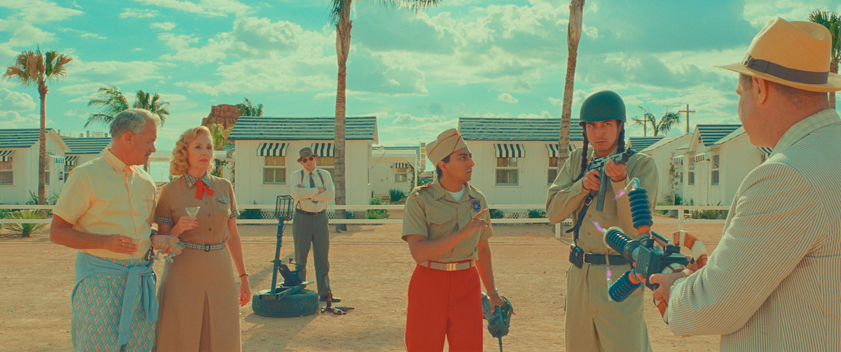 Individuals in pastel clothes stand in the desert