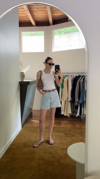 An influencer wearing relaxed denim Bermuda shorts with a white tank.