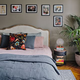 Double bed with pink and dark grey bedding, black bedside table, hanging wall art and houseplant in grey painted room