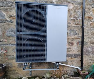 A heat pump mounted on the exterior stone wall of a UK home