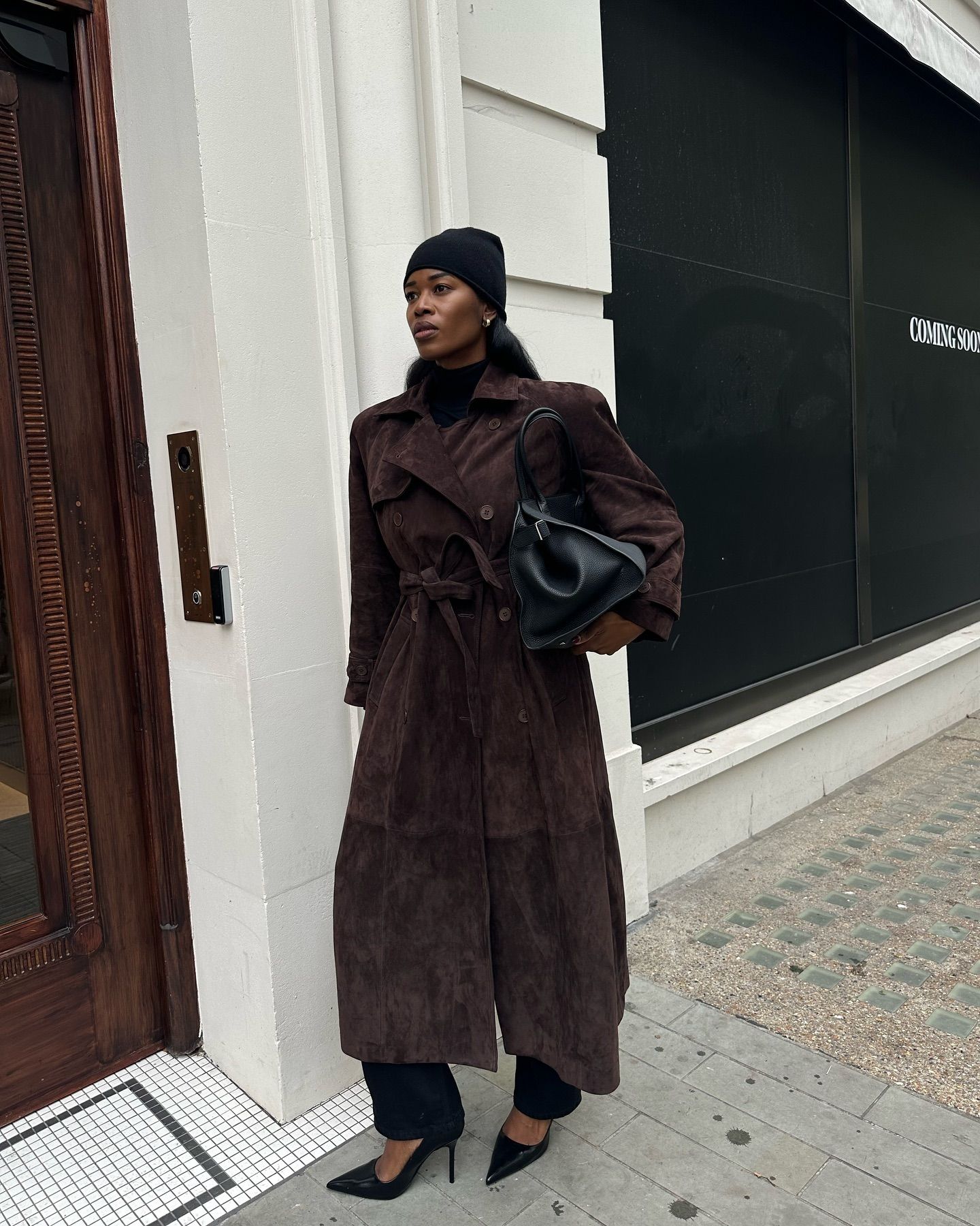 @nlmarilyn wearing a black hat, brown suede trench, black pants, and black pumps.