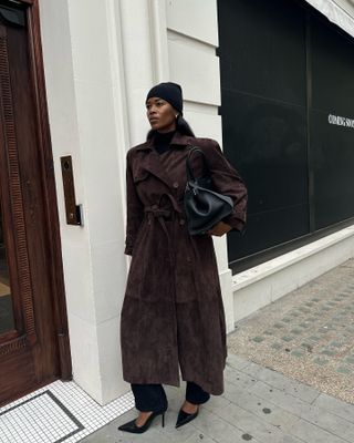 @nlmarilyn wearing a black hat, brown suede trench, black pants, and black pumps.