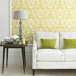White sofa and green chairs in front of yellow patterned wallpaper