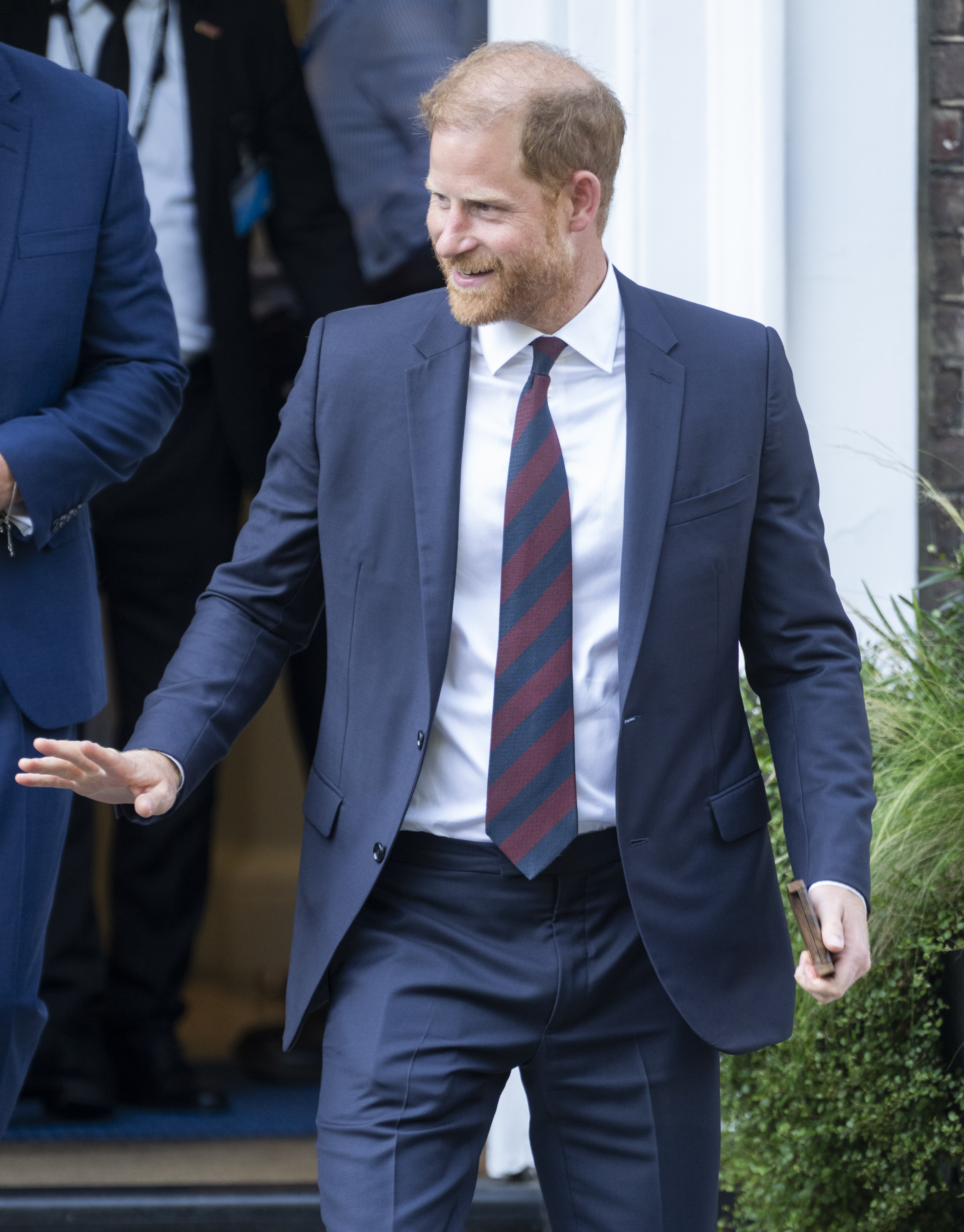 Prince Harry wearing a blue suit and tie and waving