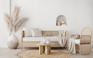 A boho style room with a wicker sofa and chair, alongside a small wooden coffee table, and a large vase containing pampas leaves.