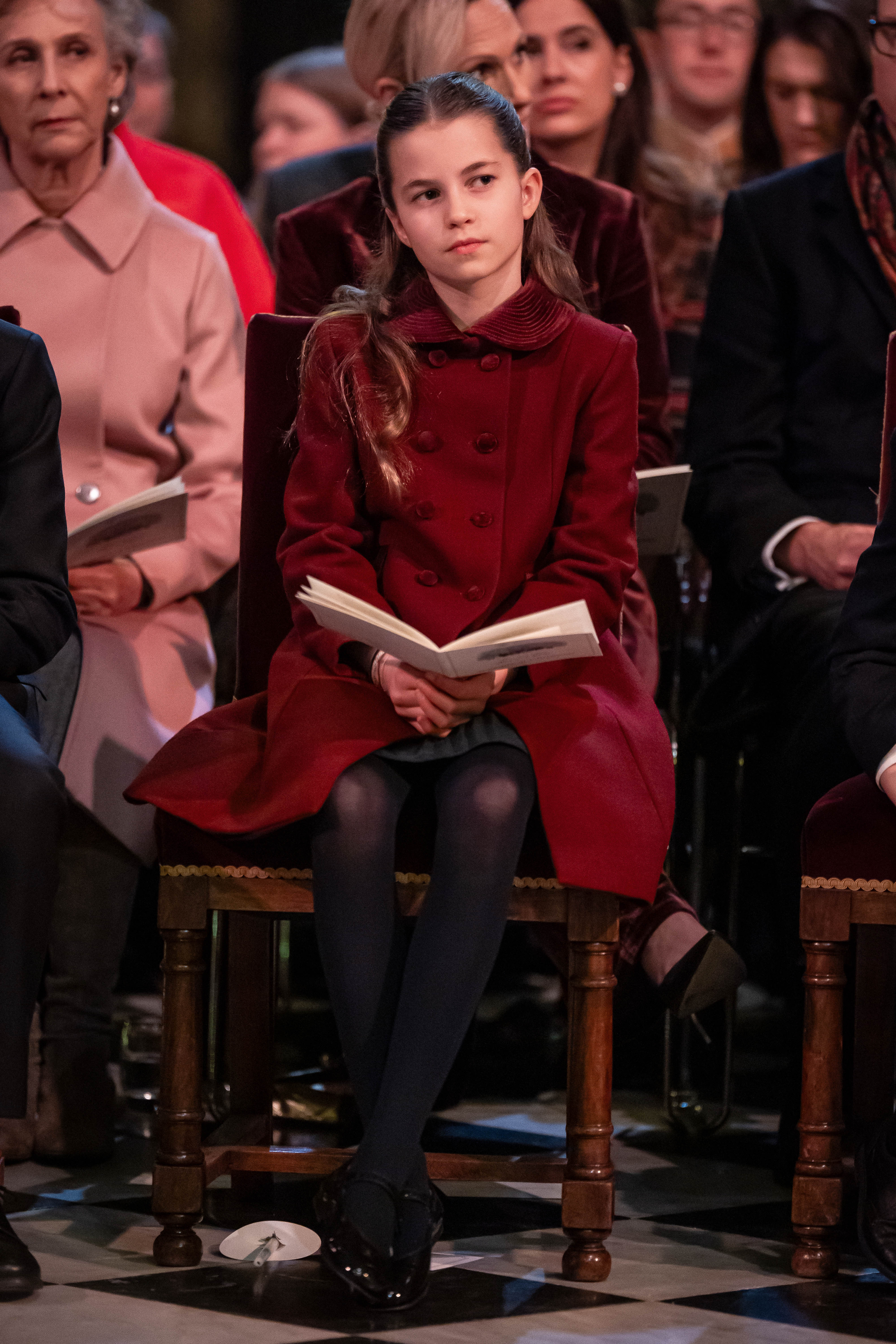 Princess Charlotte wearing a burgundy coat sitting in a chair in church